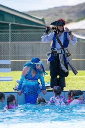 Kaz in her mermaid tail beside a pirate performer, entertaining children at a public pool event